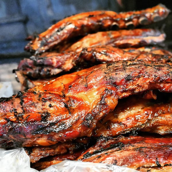 Close-up of glistening, charred BBQ ribs from A&R BBQ, stacked on a white surface.